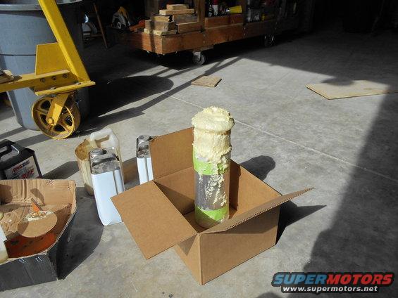 Pipe with expanding foam in a cardboard box, with jugs and a yellow lift in the background