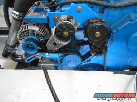 Close-up of engine components including alternator, belt tensioner, and pulleys on a blue engine block