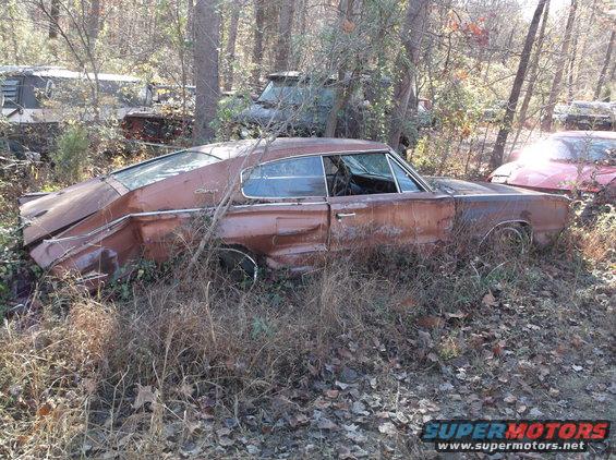Rusty 1966 Dodge Charger sits in a junkyard with other vehicles visible