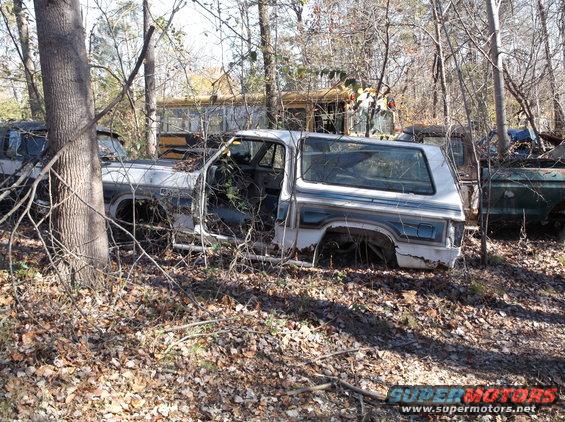 Abandoned pickup truck in a junkyard with a school bus in the background