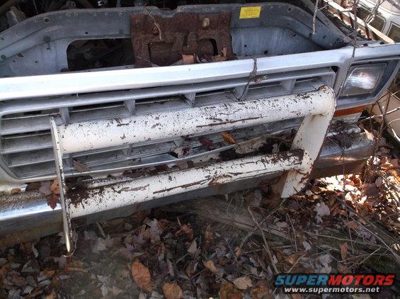 Front grille and bumper of a white 1973 Ford F-Series pickup truck, showing rust and debris