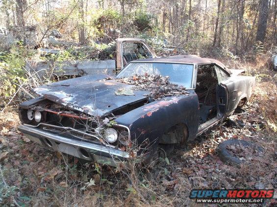 Black 1969 Dodge Charger in disrepair, front quarter view, leaves on hood, missing wheels and doors