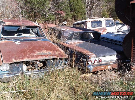 couple of rusty old cars sitting in a junkyard with tall grass