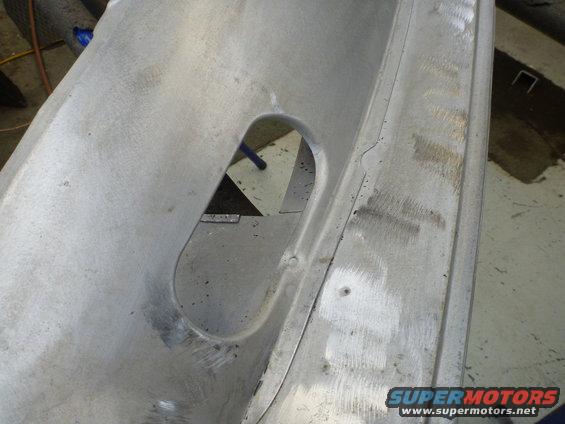 Close-up of an unfinished aluminum panel with an oval cutout and some scuff marks. Supermotors.net logo visible
