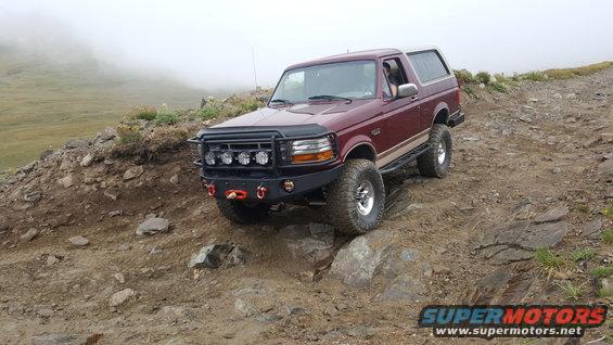 1996 Ford Bronco navigating a steep, rocky mountain path with fog in the background