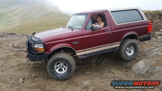 Red 1996 Ford Bronco with tan top on rocky trail
