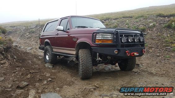 1996 Ford Bronco on a dirt and rock path with a custom front bumper and off-road lights