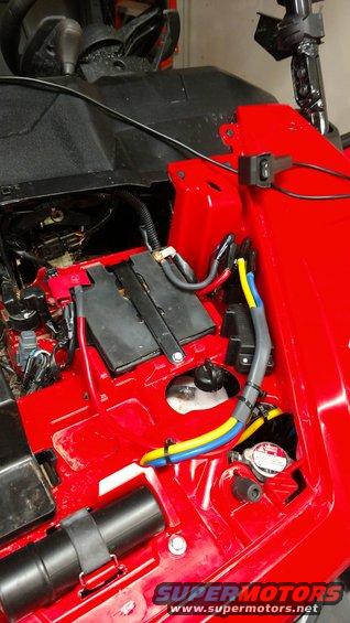 ATV battery compartment with red plastic housing, black battery, and yellow, blue, and red wires