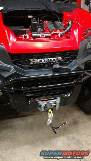 Front view of a red Honda ATV with a winch installed on the bumper. The hood is open showing engine components