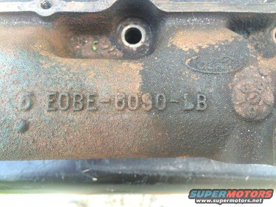 Close-up of a rusty metal engine part showing casting numbers E0BE-6090-1B and a Ford logo