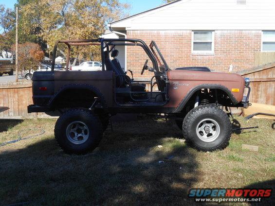 Side view of a 1972 Ford Bronco in rust brown with a roll cage and lifted suspension