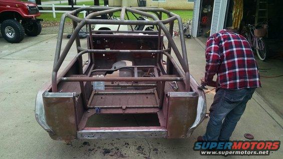 1985 Jeep CJ7 body undergoing fabrication with a roll cage installed. A red Toyota Land Cruiser is parked to the left
