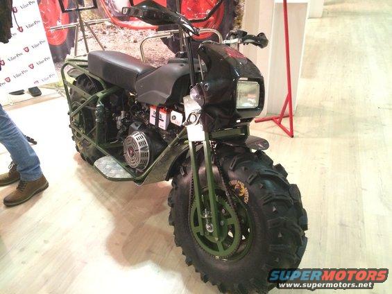 Green all-terrain motorcycle with large knobby tires and exposed engine, viewed from the front-right
