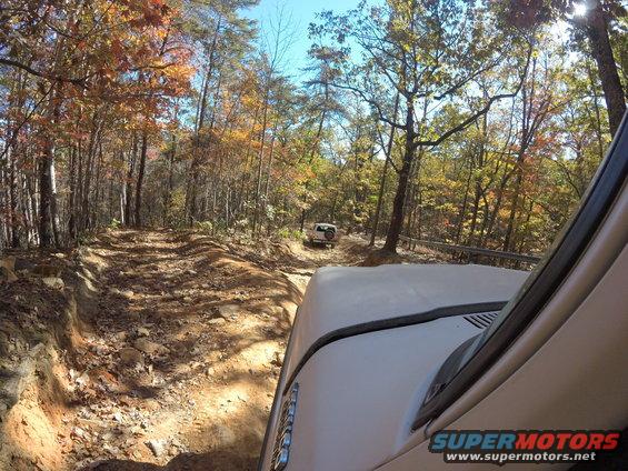 White 1979 Ford Bronco driving on a wooded trail during autumn