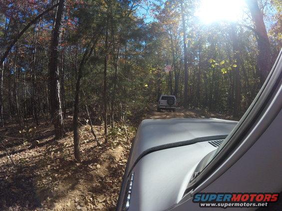 View from inside a vehicle looking at another SUV on a wooded dirt road