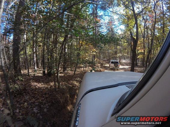 Driving on a dirt path through trees, another SUV ahead