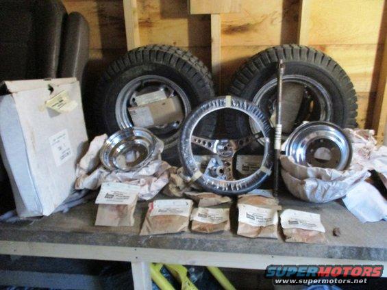 Vehicle parts including two tires on rims, a chrome steering wheel, brake rotors, and small packaged items on a shelf