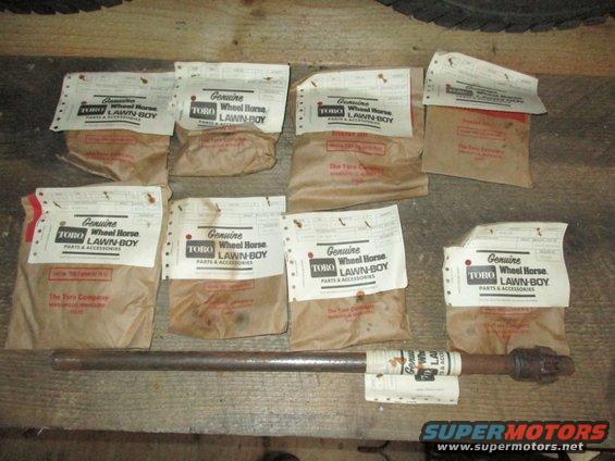 Several packages of Toro Wheel Horse Lawn-Boy parts and accessories, with a metal shaft in front