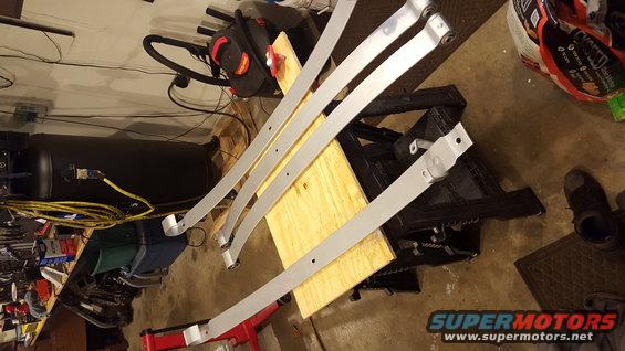Leaf springs laid out on a workbench with an air compressor in the background