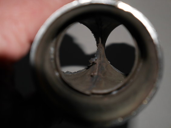 Close-up view inside a damaged exhaust pipe, showing a split and rough edges