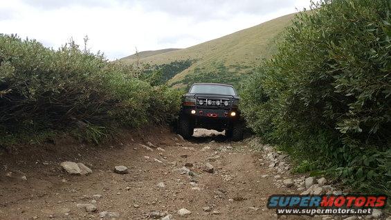 Black Ford Bronco with auxiliary lights on front grille driving on a dirt road