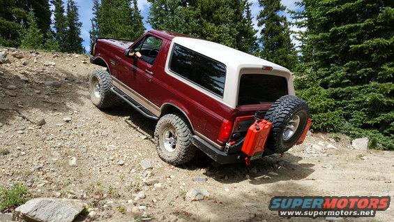 Red and white Ford Bronco with off-road tires and jerry cans on a dirt trail