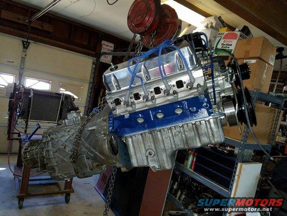 Engine and transmission assembly suspended by chains, with blue painted valve covers and silver oil pan