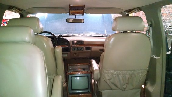 Interior of a van, showing front seats, dashboard, and a TV console