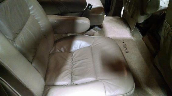 Interior of a light-colored vehicle, possibly a van or RV, with upholstered seating and overhead compartments