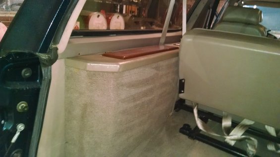 Interior view of a vehicle's rear seating area with carpet and a tan seat