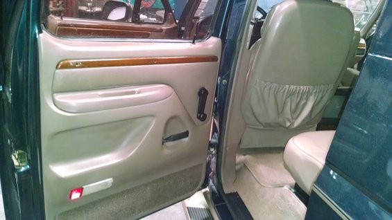 Interior of a dark green truck, showing the driver's side door panel and tan seats. Wood trim accents the door