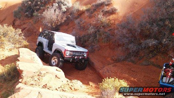 White Ford Bronco with red grille trim, off-roading on a sandy incline