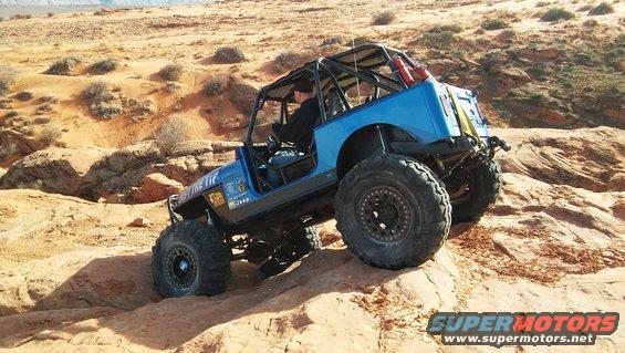 Blue Jeep with a roll cage driving over rocks in a desert landscape