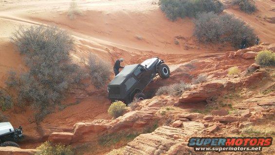 Black Jeep Wrangler climbing a rocky, sandy hill with a white Jeep visible below
