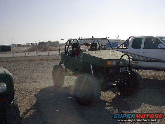 Green custom buggy with roll cage parked next to a white pickup truck
