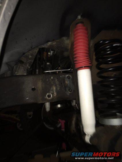 Close-up of a vehicle's front suspension with a red-booted shock absorber and black coil spring