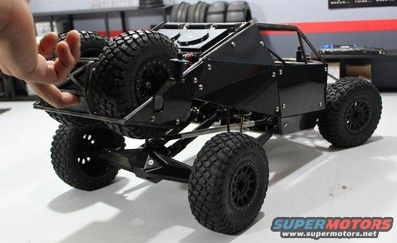 Black remote control rock crawler with spare tire mounted on rear. Hand is touching the rear cage