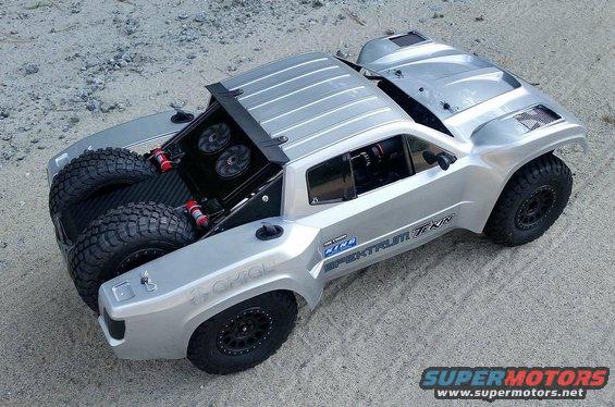 Silver remote control rock racer with two spare tires in the back. Has 'SPEKTRUM' and 'TEKIN' text on the side