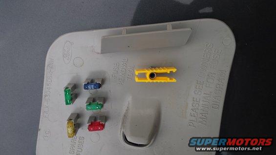 Fuse box cover with fuses and yellow fuse removal tool. Text reads 'PLEASE SEE OWNERS MANUAL FOR FUSE DIAGRAM'