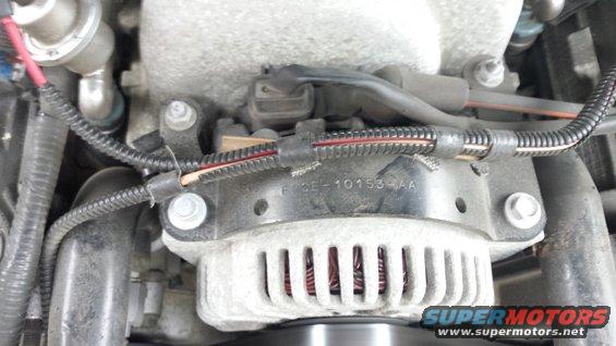 Close-up of car engine parts, showing alternator and wiring harness. Part number F7DE-10153-AA visible