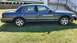 1995 Mercury Grand Marquis - A dark sedan is parked on a grassy lawn, viewed from the side, with visible damage to its front bumper.