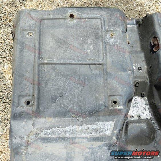 Close-up of a dark gray, rectangular car part with mounting holes and some white residue