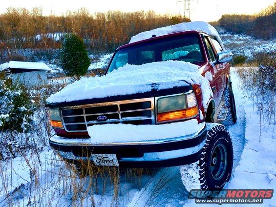 Red Ford Bronco covered in snow, front 3/4 view, parked on a snowy path