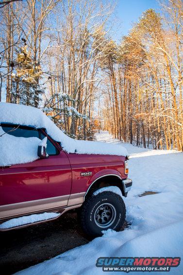 Red Ford Bronco with snow on its roof and hood, parked on a snowy driveway
