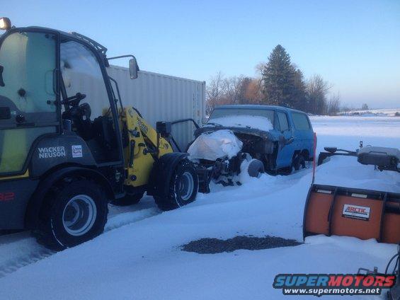 Blue SUV with front end damage in snow, next to a Wacker Neuson loader and a snow plow