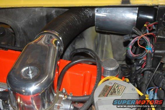 Close-up of engine bay showing chrome air cleaner, orange valve cover, black hose, and wiring harness. An ACCEL ignition component is visible