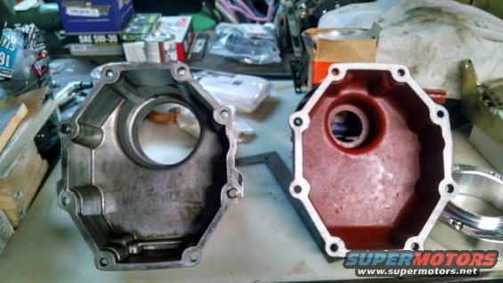two metal engine covers, one silver and one red, on a workbench with tools and boxes in the background. Supermotors logo visible