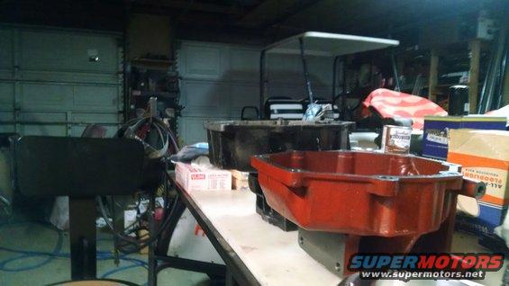 Two oil pans, one red and one black, sit on a workbench in a garage. A golf cart is visible in the background