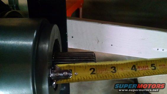 Close-up of a splined shaft being measured with a yellow tape measure against a white wooden beam