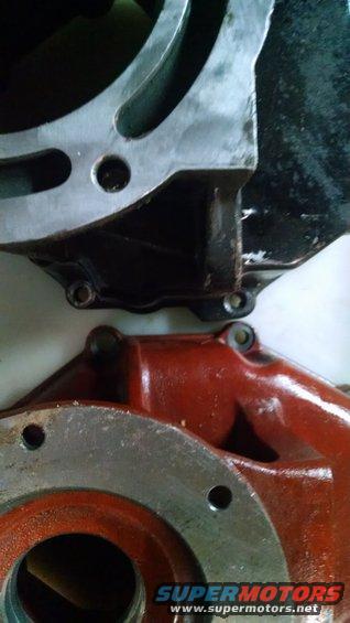 close-up of two metal engine components, one black and one red, with bolt holes visible